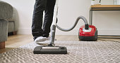 Carpet, vacuum cleaner and a person cleaning in a home lounge for dust, dirt and maintenance. Legs closeup of an adult with an electric appliance for vacuuming the living room floor in a clean house