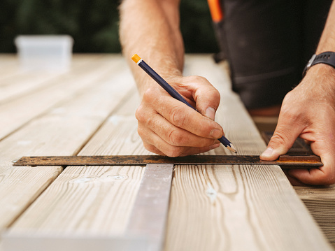 Man measuring and building a wooden patio deck outdoors in his garden\nWorking and buidling under contstruction. Home improvement.