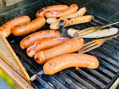 Stock photo showing close-up, elevated view of a barbecue in a garden setting. Pictured cooking on the barbecue are some sausages.