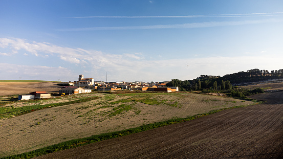 Surrounded by farmland, a small village in the province of Valladolid-Spain in the early morning hours. A drone view with a blue sky with little cloud cover, a small paraglider can be seen.
