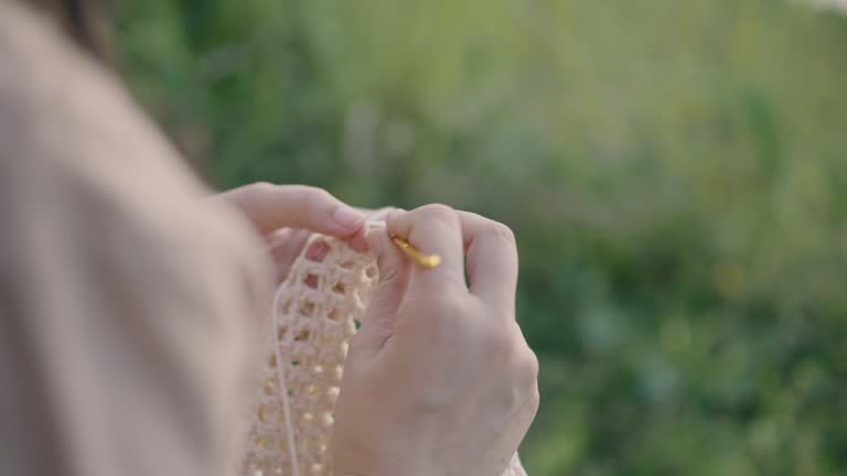 Young woman resting at river bank and enjoying crocheting in the Nature.