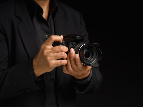 Photographer with a camera. Close-up of hand holding the digital camera while standing on a black background. Space for text