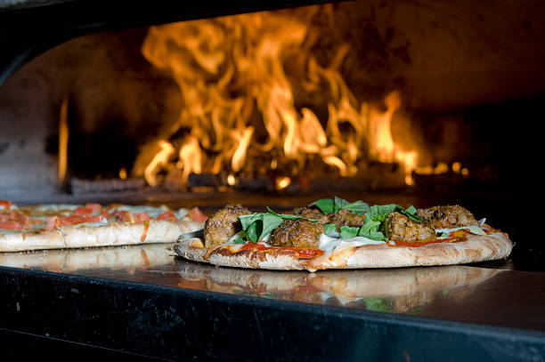 A fire baked meatball pizza on the edge of the oven with the fire in the background.