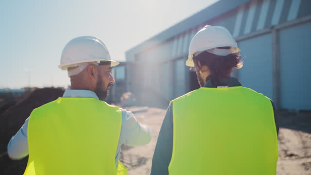 Back, planning and construction worker with an architect walking on a building site for discussion or inspection. Meeting, teamwork or collaboration with an engineer talking to an industry designer