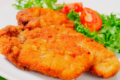 big fried breaded Wiener schnitzel (escalope) with vegetable garnish on a white plate