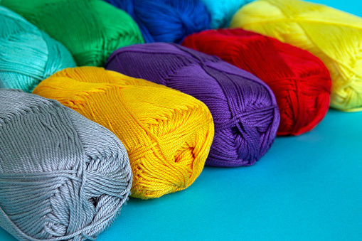 Colorful multi-colored skeins of cotton yarn are folded in a row at an angle. Materials for knitting. Textile industry. Small depth of field.