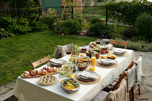 Group of chairs surrounding long table served with fresh and healthy homemade food and drinks prepared for outdoor family dinner