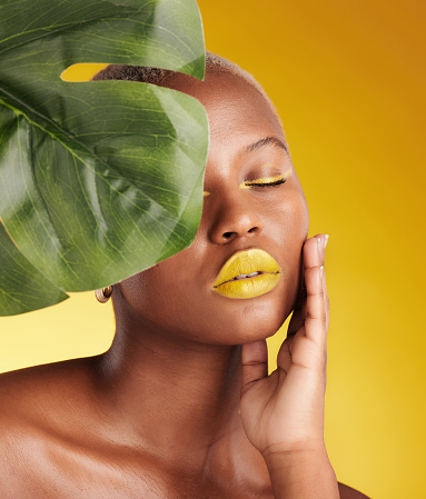 Beauty, makeup and leaf with face of black woman in studio for tropical, natural and cosmetics. Luxury, sustainability and health with female model on yellow background for plant, salon and wellness