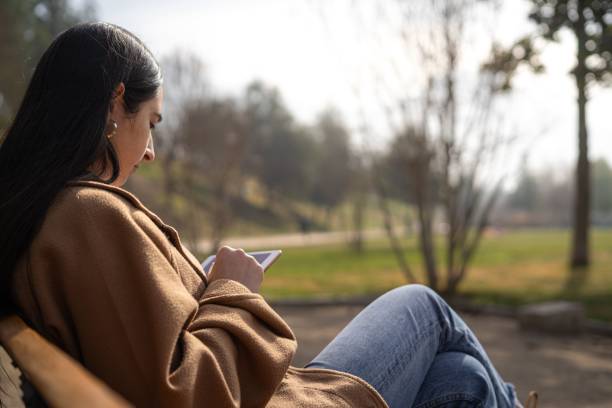 istock Young woman with a disability sitting on a park bench using a digital tablet for work 1585026548
