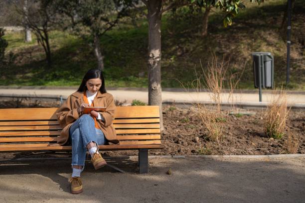 istock Young woman with a disability sitting on a park bench using a digital tablet for work 1585027074
