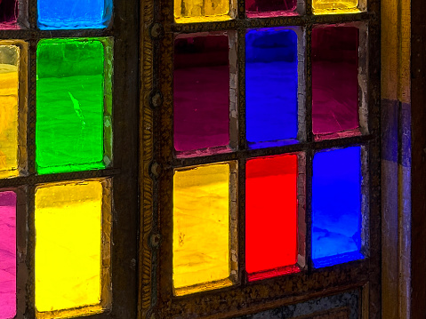 Stock photo showing close-up view of heavy wood door with square, multi-coloured stained glass panels.