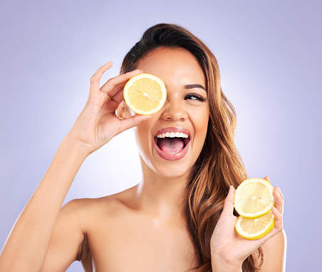 Vitamin c, lemon and eye of woman with detox, natural or organic beauty isolated in a purple studio background. Excited, happy and young female person with vitamin c for healthy skincare or wellness