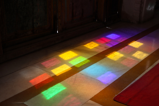 Stock photo showing close-up view of light flowing through stained glass panels projecting multicoloured rectangles onto the floor.