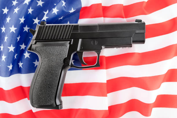 istock Black pistol gun over American flag. Firearms restriction debate. 1585050978