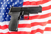 Black pistol gun over American flag. Firearms restriction debate.