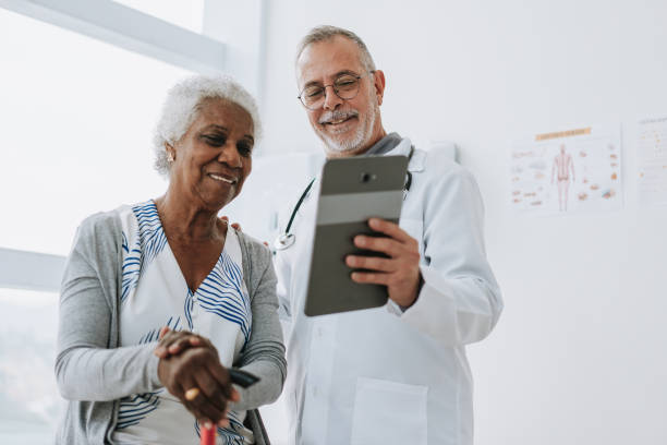 medico che assiste il paziente anziano utilizzando la tavoletta digitale - patient retirement senior adult hospital foto e immagini stock