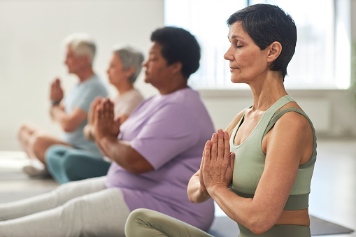 Group of people sitting in lotus position and meditating in yoga class