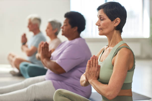 People meditating in yoga class Group of people sitting in lotus position and meditating in yoga class meditating stock pictures, royalty-free photos & images