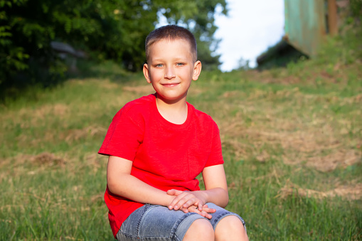A boy in a red T-shirt sits on the background of summer nature.