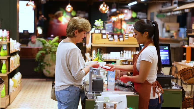 Latin American mature woman shopping at the supermarket and making a contactless payment with her credit card