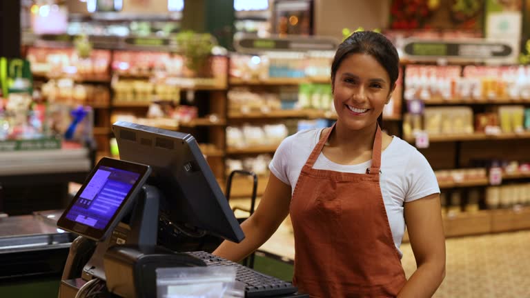 Latin American beautiful cashier facing the camera smiling while standing behind the cash register