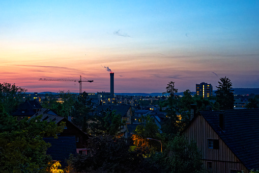 Dramatic colorful evening sky at City of Zürich district Schwamendingen with skyline, crane and chimney on a sunny spring day. Photo taken May 29th, 2023, Zurich, Switzerland.
