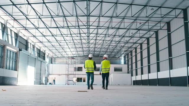 Teamwork, construction or planning with an an engineer and designer in a warehouse for building or architecture. Back, walking or engineering with an architect and builder talking industry strategy