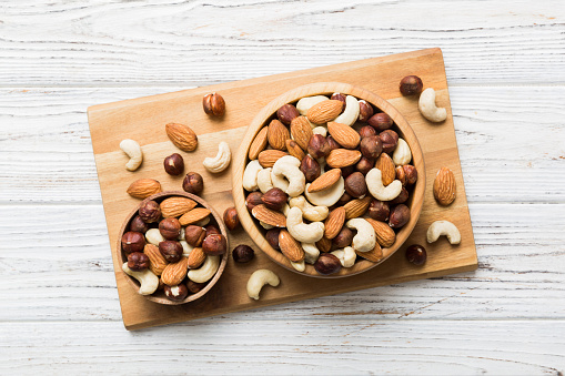 Assortment of nuts in wooden bowl on colored table. Cashew, hazelnuts, walnuts, almonds. Mix of nuts Top view with copy space.