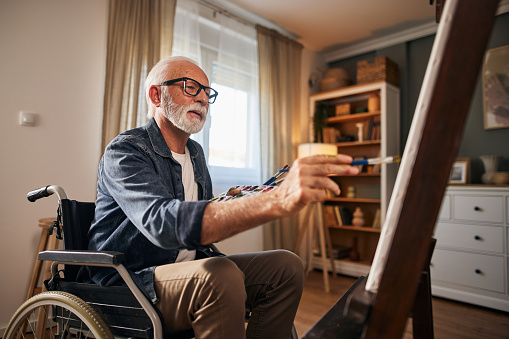 Senior man in a wheelchair painting at home