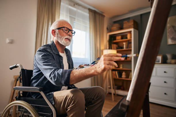 homem idoso em uma cadeira de rodas pintando em casa - art freedom paintbrush painting - fotografias e filmes do acervo