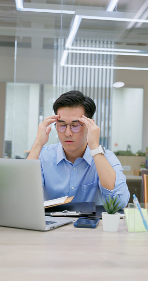 pain at work - stressed asian businessman suffer from headache while he using laptop computer in office