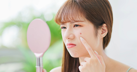 asian beauty woman hold mirror feel worried pointing acne on her cheek at home