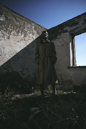 a person standing in front of a wall wearing a gas mask and trench coat, in the grass, low angle shot, good for book cover