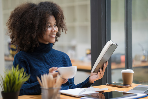 African American businesswoman drinking a coffee and reading a book at the office.