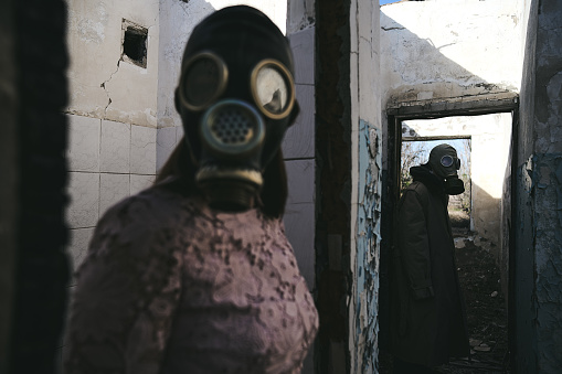 the woman in a gas mask staying in front of a man in destroyed building, good for book cover