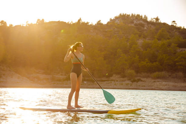 istock SUP Stand up surf girl with paddle at sunset 1585192953