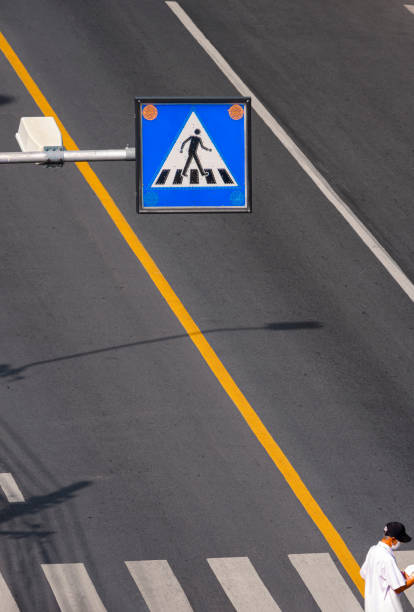 Bangkok, Thailand - April 13,2021: Selective focus at overhead electric pedestrian crossing sign with elderly man is walking on zebra crosswalk in vertical frame