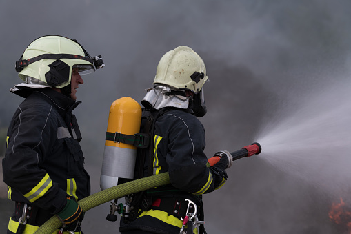 Firefighters using water fog type fire extinguisher to fighting with the fire flame to control fire not to spreading out. Firefighter industrial and public safety concept. High quality photo