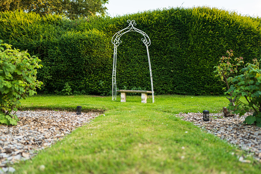 Wrought iron garden arbor and bench located at the edge or an ornate garden at an English stately home.