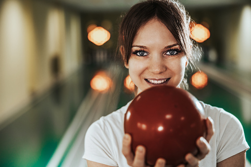 Portrait of a cute young woman holding bowling ball at the bowling club. Looking at camera.