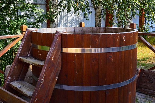 Photo of wooden barrel with ladder for swimming after bath. Steam room. Vacation in country.