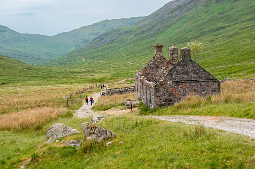 Fort William, Scotland - June 17, 2022: Hikers on the West Highland Way in the Scottish Highlands with an abandoned farmhouse.
