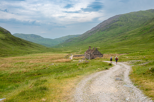 Fort William, Scotland - June 17, 2022: Hikers on the West Highland Way in the Scottish Highlands with an abandoned farmhouse.
