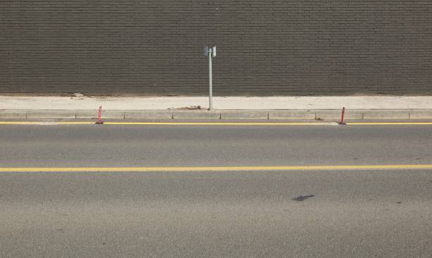 istock Concrete sidewalk with metallic pole. Black brick wall on behind, street in front. 1585307581