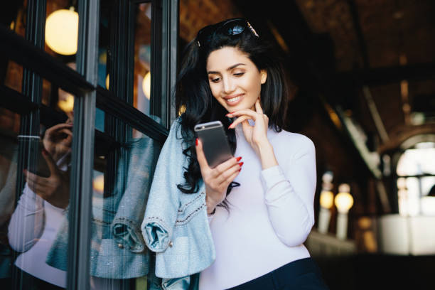 istock Gorgeous brunette in sunglasses, formal attire, flirting online, waiting for response joyfully at cafe. 1585351302