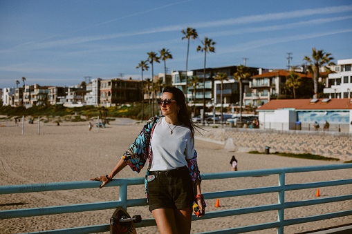 Woman spending an afternoon at the Los Angeles Manhattan beach, relaxing and enjoying the sunshine, carrying a longboard.