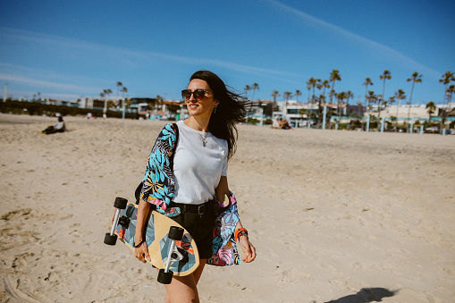 Woman spending an afternoon at the Los Angeles Manhattan beach, relaxing and enjoying the sunshine, carrying a longboard.