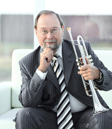 Musician with saxophone  against a grey backdrop. Man looking down, serious wearing a black hat and shirt