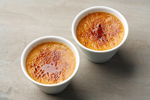Creme brulee with caramel in two white bowls on gray background close up