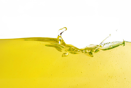 Beauty and allure of a stunning wave of yellow base oil, emanating a sense of motion and vitality on a pristine white background. The liquid's transparent and golden-colored splashes create an abstract and visually captivating display, representing the crucial role of lubrication in both automotive and industrial sectors.
